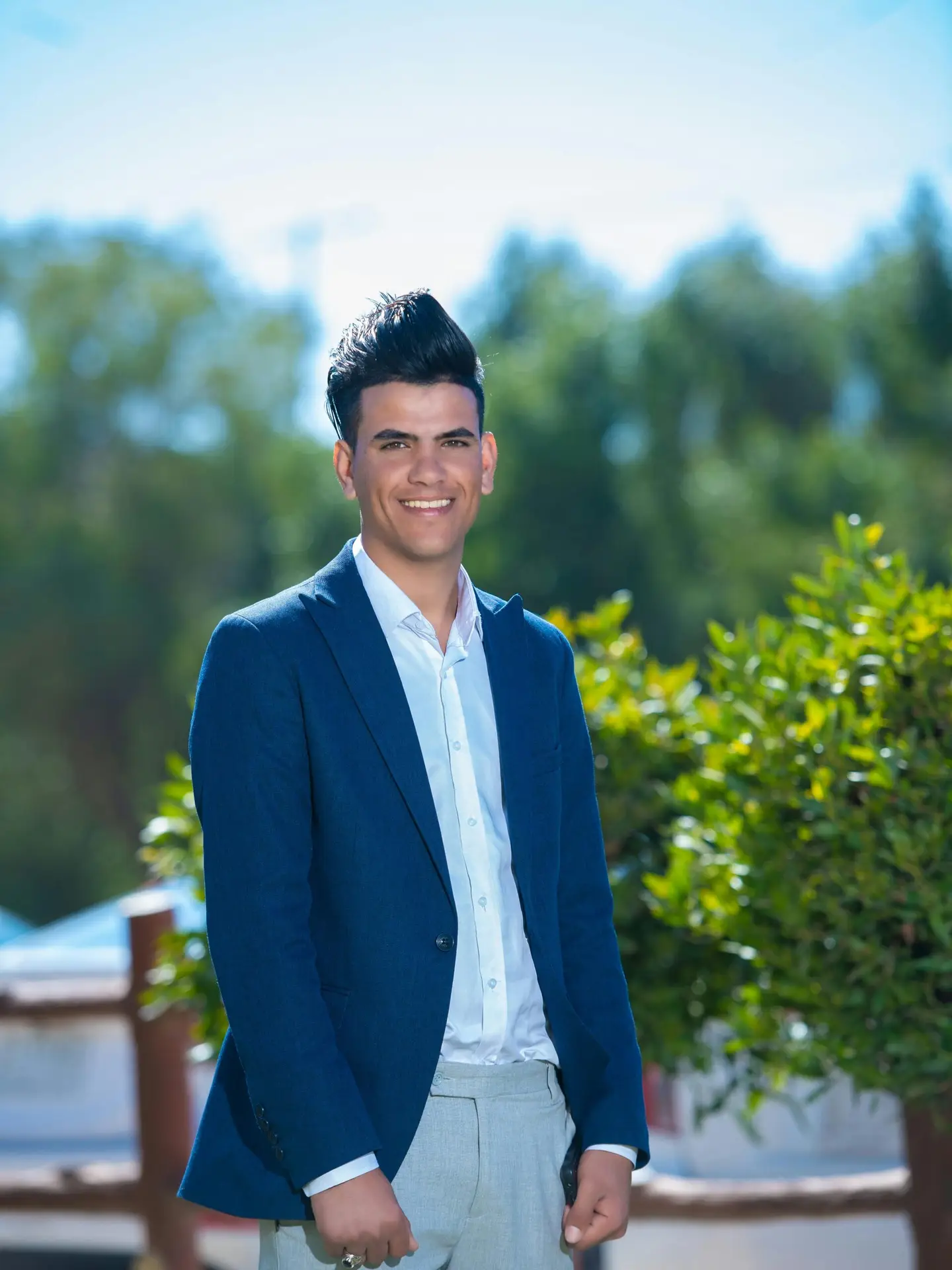 Portrait of a young man in a blue suit smiling outdoors on a sunny day.